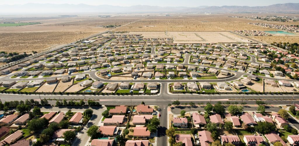 Aerial view of a suburban neighborhood with neatly arranged homes and streets, surrounded by arid terrain and distant mountains.