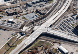Aerial view of a complex highway interchange with multiple lanes and intersecting routes, surrounded by parking lots and buildings.