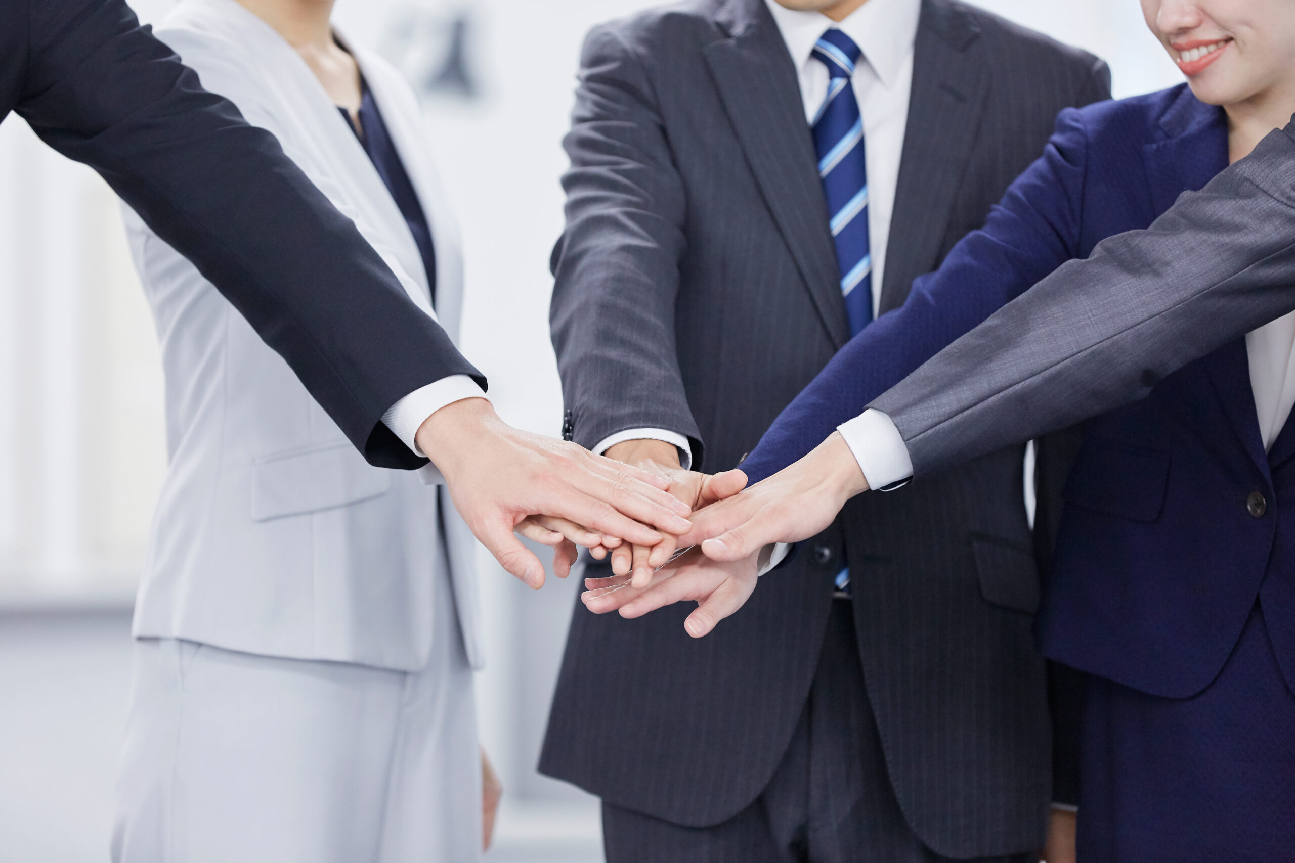 Business professionals in formal attire join hands in a team gesture, symbolizing collaboration and unity in a corporate setting.