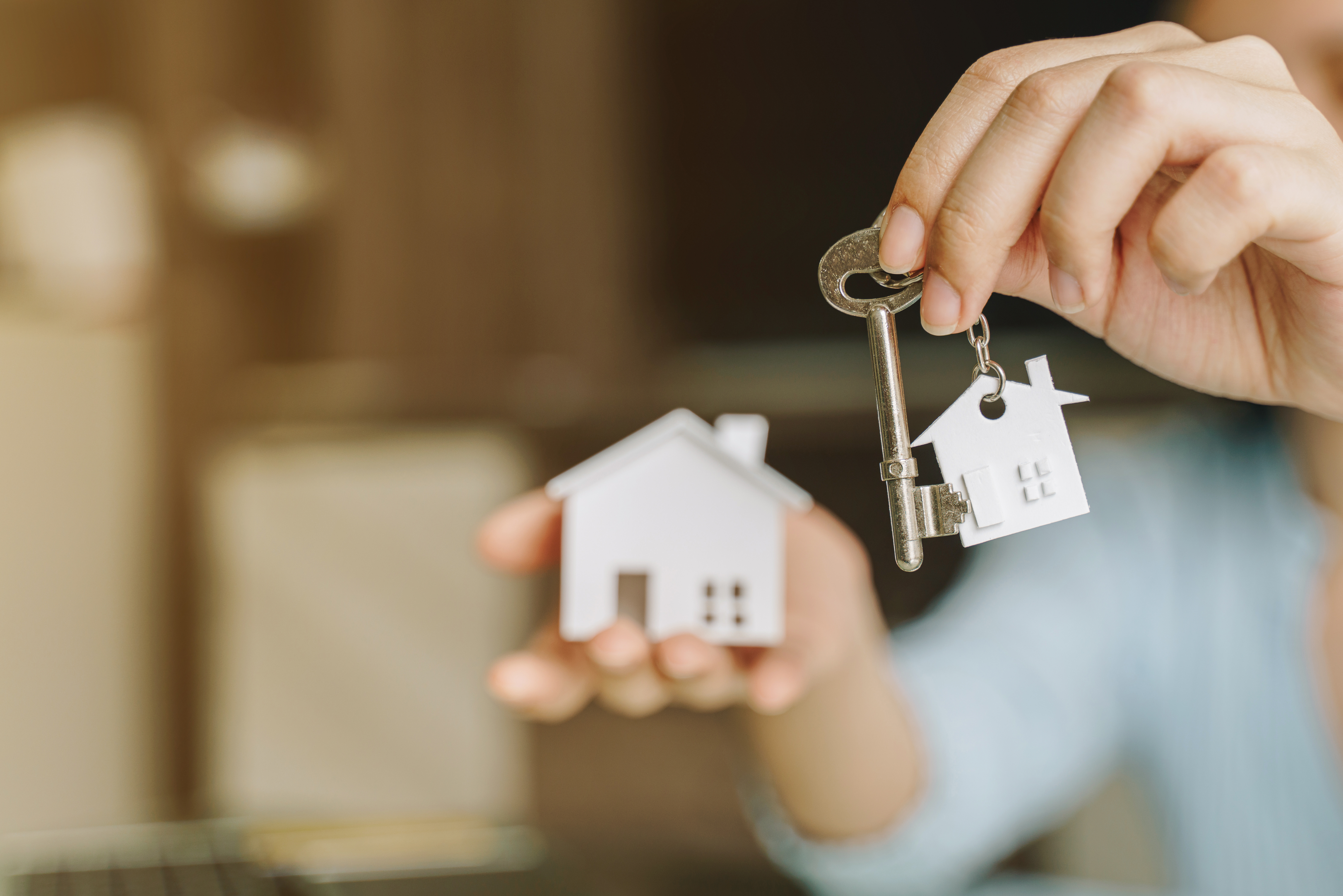 Hand holding a key and a white house-shaped keychain, symbolizing home ownership and real estate opportunities.
